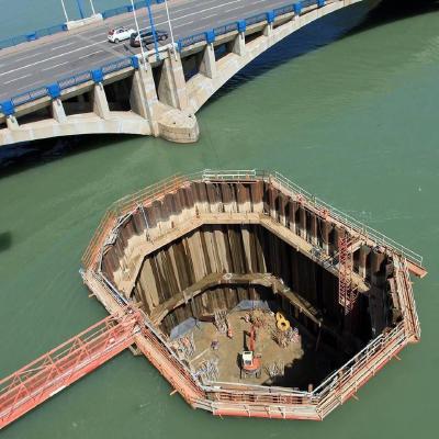 A picture of an excavation happening on a river bed, showing a hole with reinforced metal sides holding the water back